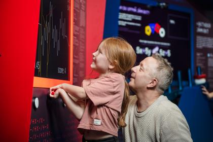 En flicka och hennes pappa utforskar en monter inne i utställningen Mathrix.