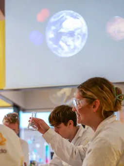 Fyra personer sitter i ett kemilabb, i bakgrunden syns jorden på en projektorduk.