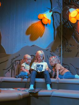 Tre barn sitter och läser böcker nere i Miniverseum, en upplevelse för Universeums yngsta besökare.