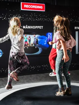 Tre äldre barn hoppar Månhoppet inne i utställningen Rymdresan.