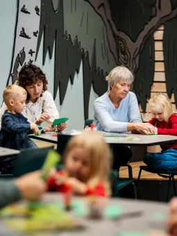Två barn och två vuxna klipper och klistrar i miniverseum.