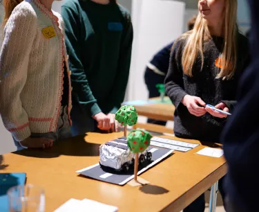 En grupp ungdomar står runt ett bord och tittar på en modell.