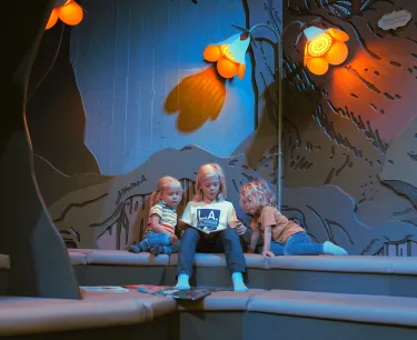 Tre barn sitter och läser böcker nere i Miniverseum, en upplevelse för Universeums yngsta besökare.