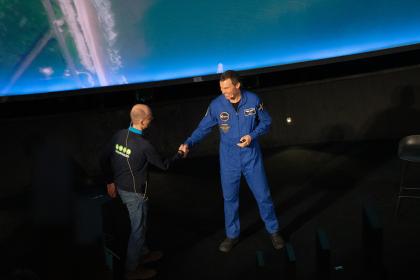 Två män som hälsar på varandra, den ena bär astronautkläder. 