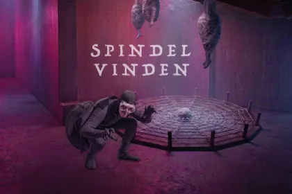 En person utklädd till spindel står framför ett spindelnät. Kokonger hänger i taket.