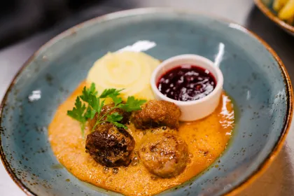 En portion med köttbullar, mos, sås och lingonsylt ligger vackert upplagt på en härligt blå tallrik.