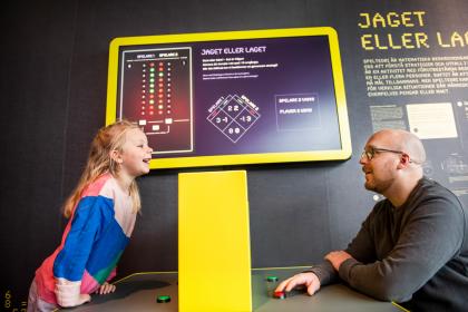 En pappa och hans barn spelar Jaget eller laget, en interaktiv monter inne i Mathrix.