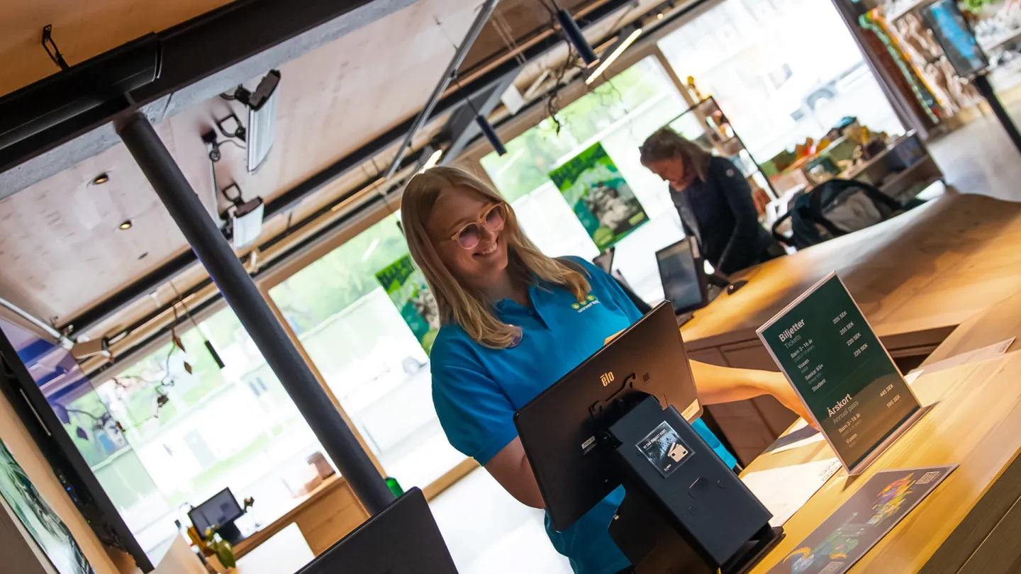 Universeum personal står bakom en kassa och ler.