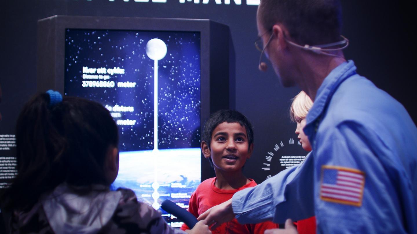 En guide visar montern "cykla till månen" för några entusiastiska barn inne i utställningen Rymdresan.