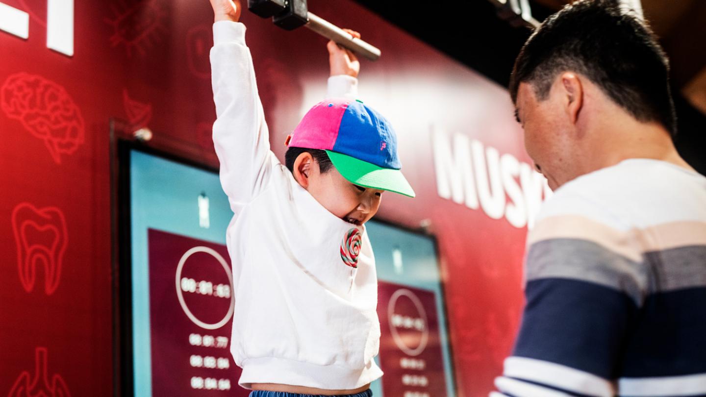 En pojke provar sina muskler genom att hänga i en stång inne i utställningen Humans.