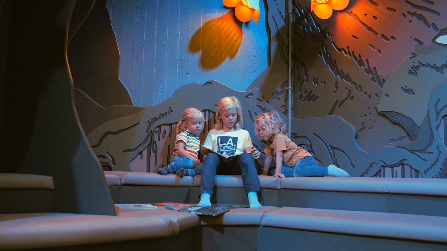 Tre barn sitter och läser böcker nere i Miniverseum, en upplevelse för Universeums yngsta besökare.