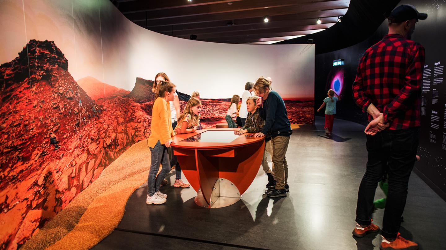 Några äldre barn står lutade över en monter som visar vad som gömmer sig på Mars inne i utställningen Rymdresan.